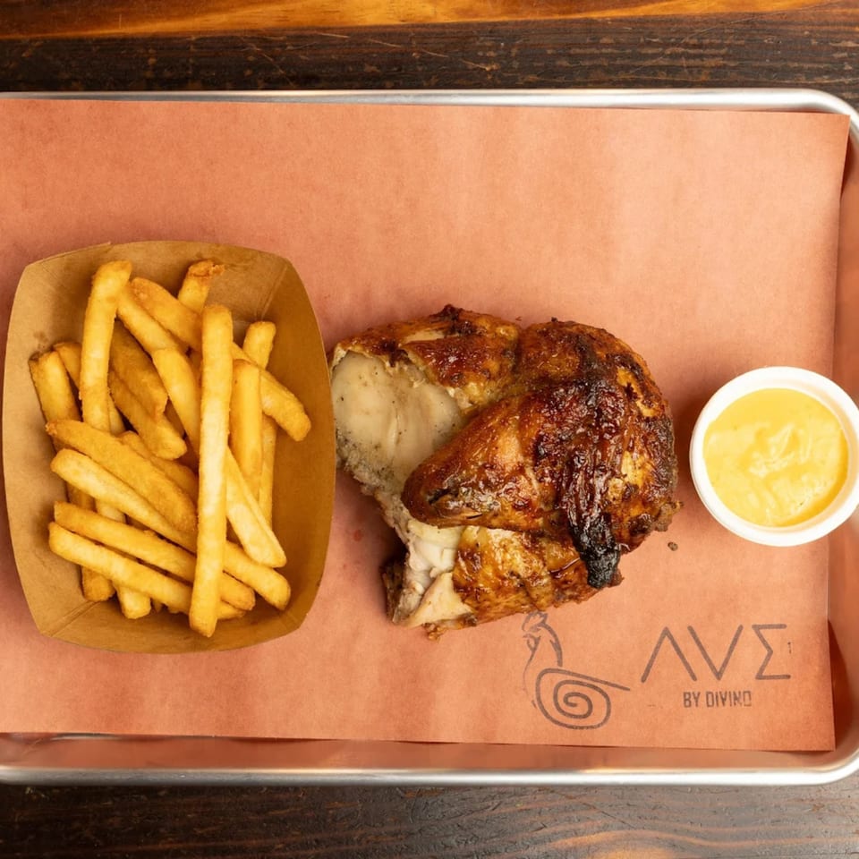 Peruvian rotisserie chicken with crispy fries and a side of yellow dipping sauce on a tray.