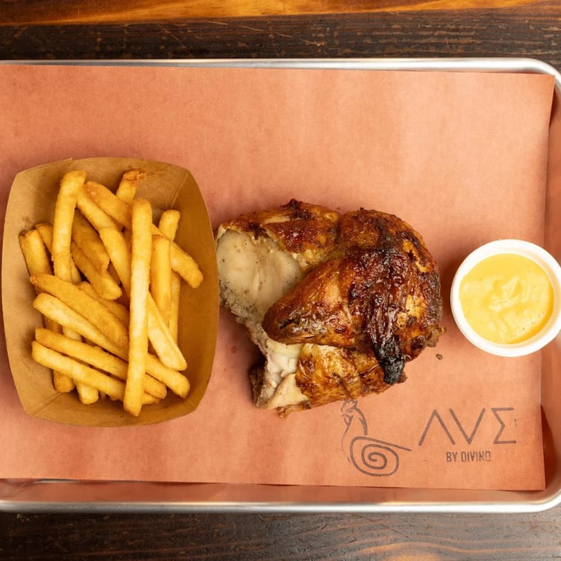 Peruvian rotisserie chicken with crispy fries and a side of yellow dipping sauce on a tray.