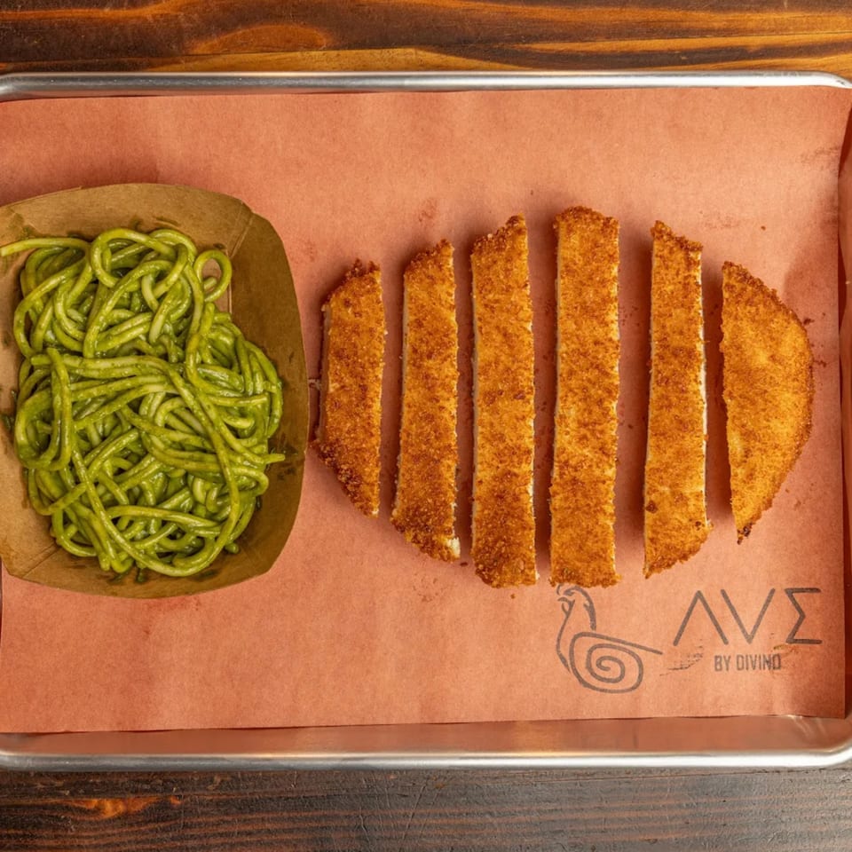 Green spaghetti and breaded fish sticks on a brown paper-lined metal tray, with the Ave By Divino logo.