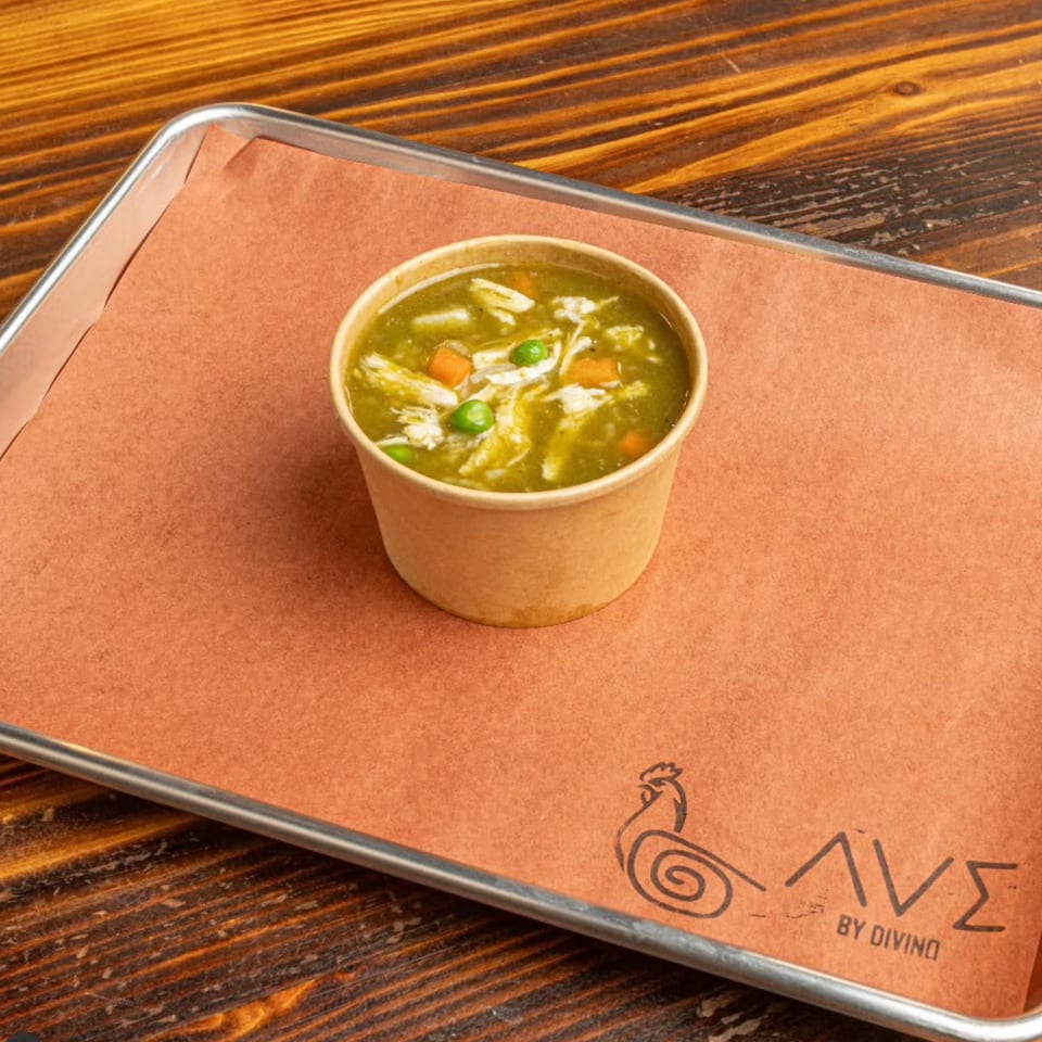 Peruvian green chicken soup with peas and carrots in a cup on a branded tray.