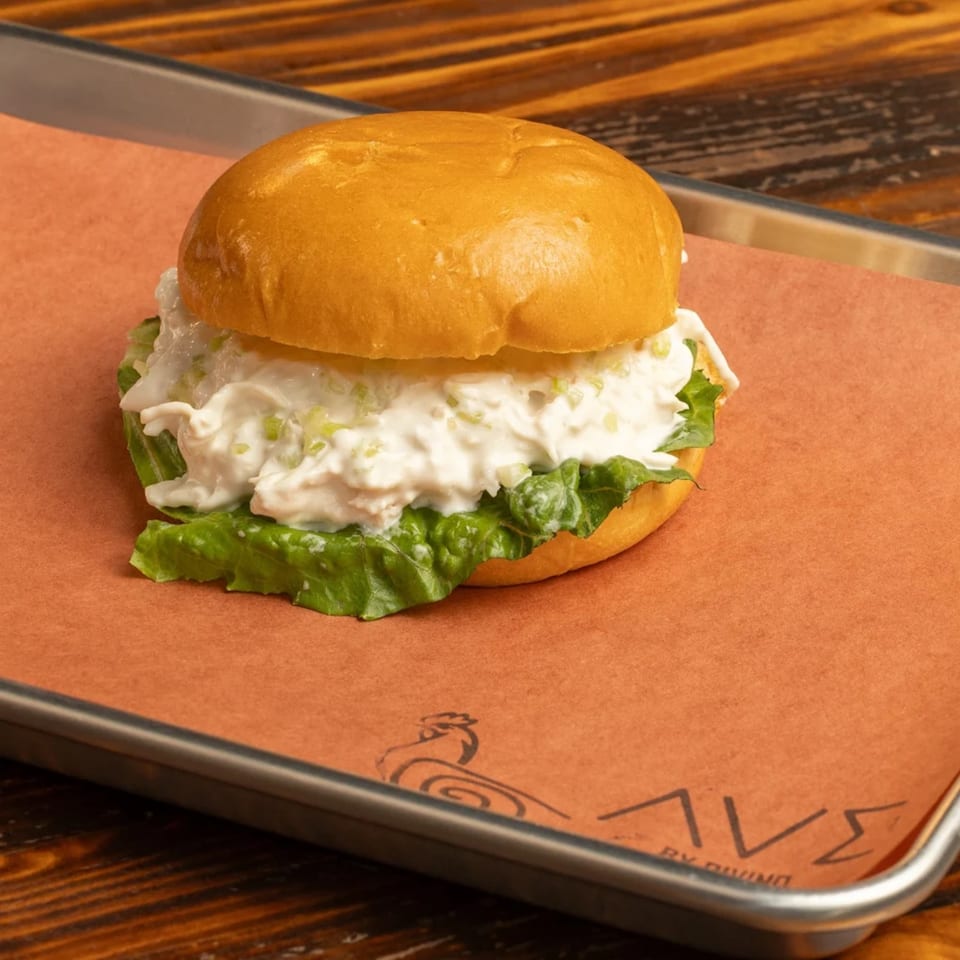 A chicken salad sandwich with lettuce on a bun, served on Ave By Divino branded paper.