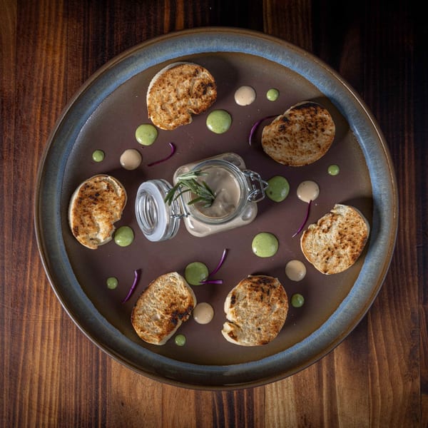 Peruvian pate in a jar with rosemary, surrounded by toasted bread and colorful sauces on a plate.