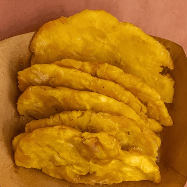 Golden fried plantains, a Peruvian side dish from Ave By Divino, served in a brown paper container.