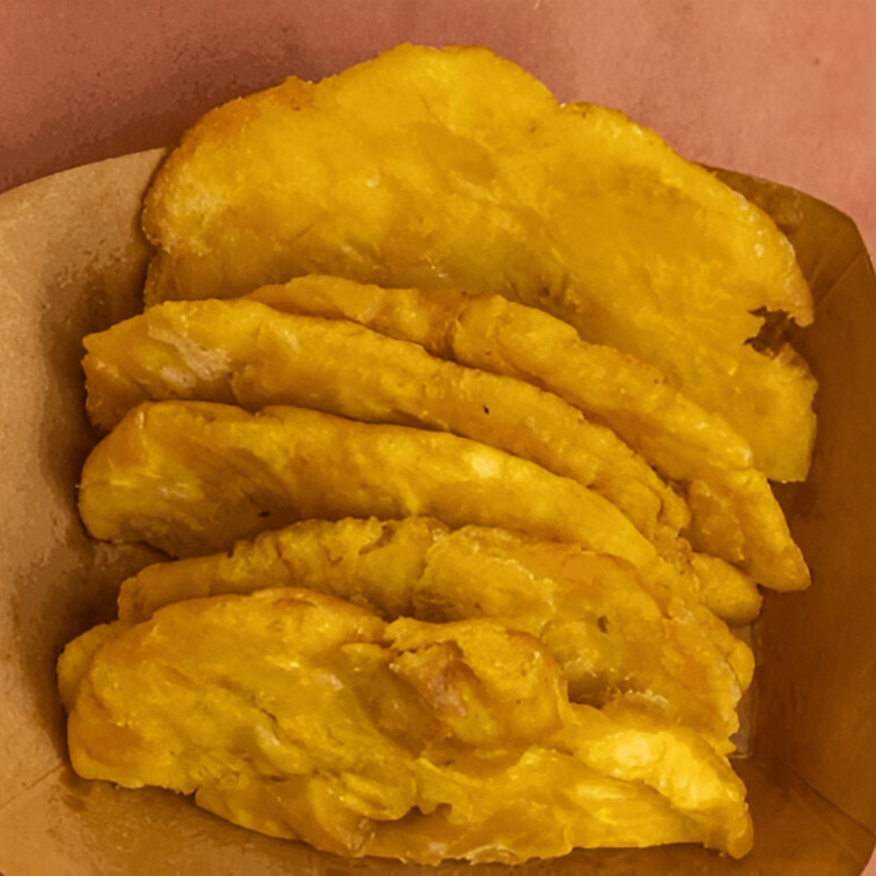 Golden fried plantains, a Peruvian side dish from Ave By Divino, served in a brown paper container.