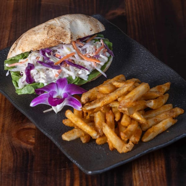 Peruvian sandwich with coleslaw and lettuce, served with seasoned fries and a purple orchid.