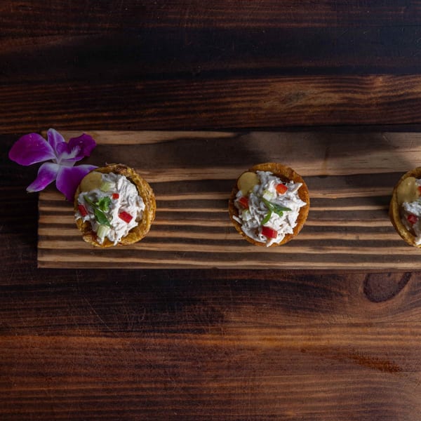 Three Peruvian chicken salad appetizers in crispy cups, garnished with red pepper and cilantro, on a wooden board.