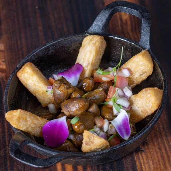 Peruvian anticuchos, grilled beef heart skewers, with golden fried yuca, salsa criolla, and purple orchid petals.