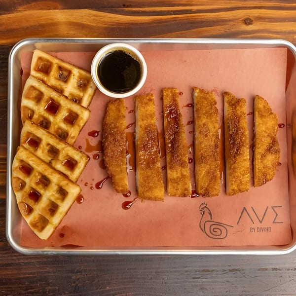 Ave By Divino's chicken and waffles, with syrup, on a metal tray with pink paper.