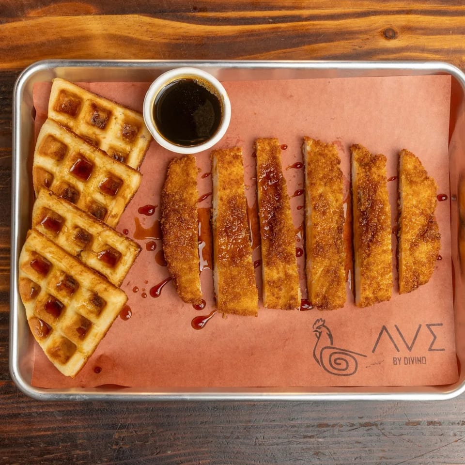 Crispy chicken strips and waffles with syrup on a tray, Ave By Divino logo visible.