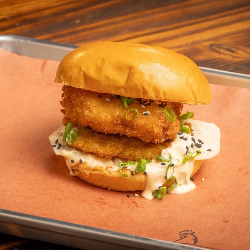 Crispy fried chicken sandwich with creamy sauce, green onions, and sesame seeds on a bun.