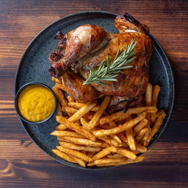 Peruvian rotisserie chicken with crispy fries and a side of yellow dipping sauce on a dark plate.